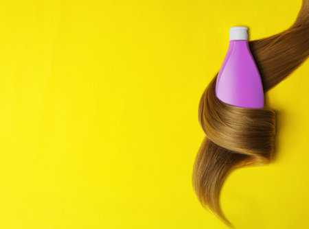 Shampoo bottle wrapped in lock of hair on yellow background, flat lay with space for text. natural cosmetic productsの写真素材