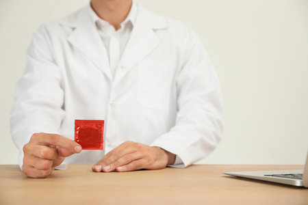 Doctor holding condom at wooden table, closeup. safe sex conceptの写真素材