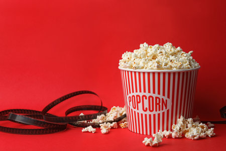 Bucket of fresh popcorn and film footage on red background, space for text. cinema snackの写真素材