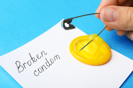 Woman piercing condom with pin on blue background, closeup. safe sexの写真素材