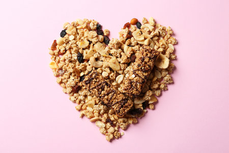 Heart made of healthy granola bars and ingredients on pink background, flat layの写真素材