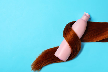 Shampoo bottle wrapped in lock of hair on light blue background, flat lay with space for text. natural cosmetic productsの写真素材