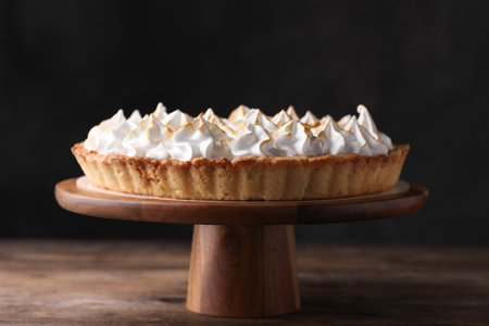 Stand with delicious lemon meringue pie on wooden table against black backgroundの写真素材