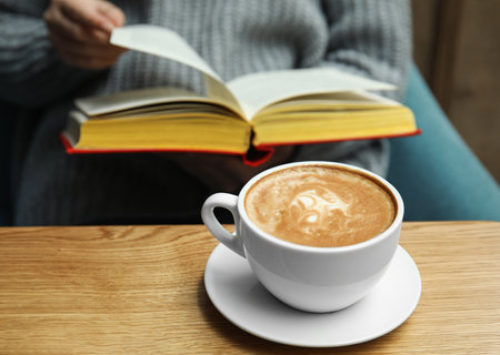 Woman reading book at table, focus on cup of coffeeの写真素材