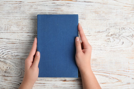 Woman holding hardcover book on white wooden background, top viewの写真素材