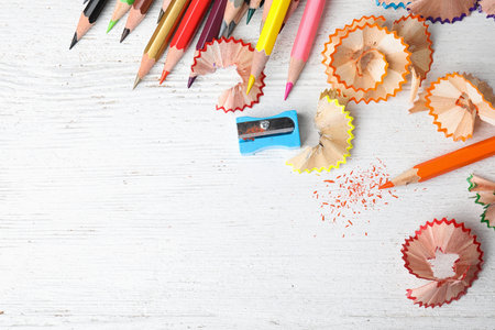 Color pencils, sharpener and shavings on white wooden table, flat lay. Space for text
