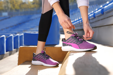 Sporty woman tying shoelaces before running at stadium