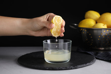 Woman squeezing lemon juice into glass bowl at gray table, closeup