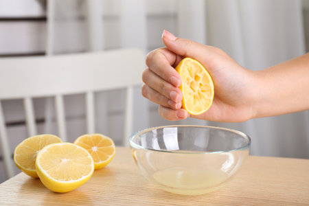 Woman squeezing lemon juice into glass bowl at wooden table, closeupの写真素材
