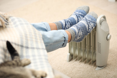 Woman warming feet on electric heater at home, closeupの写真素材
