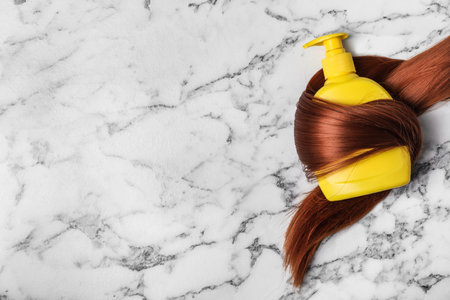 Shampoo bottle wrapped in lock of hair on white marble background, flat lay with space for text. natural cosmetic productsの写真素材