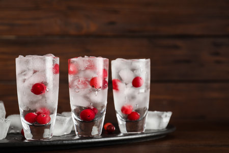 Shot glasses with vodka, ice and cranberries on table against wooden backgroundの写真素材
