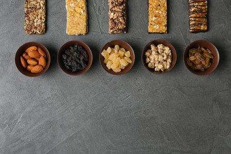 Healthy granola bars and bowls with ingredients on gray table, flat lay. Space for textの写真素材