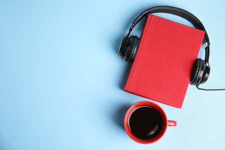 Modern headphones with hardcover book and coffee on light blue background, top view. Space for textの写真素材