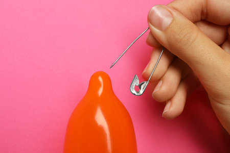 Woman piercing inflated condom with pin on pink background, closeup. safe sexの写真素材