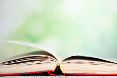 Open book on white wooden table against blurred green background, closeup. Space for textの写真素材