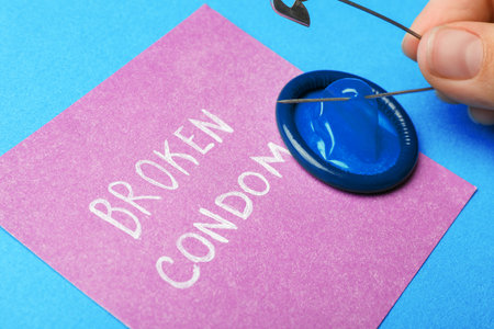 Woman piercing condom with pin on blue background, closeup. safe sexの写真素材