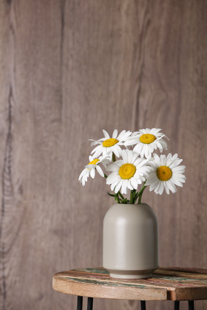 Beautiful tender chamomile flowers in vase on table against wooden backgroundの写真素材