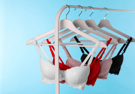 Hangers with beautiful lace bras on rack against blue background. Stylish underwearの写真素材
