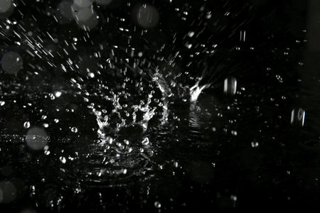 Rain drops falling down into puddle on dark backgroundの写真素材