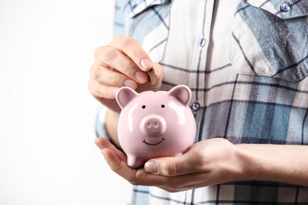 Woman putting coin into piggy bank on light background, closeup. money savingsの写真素材