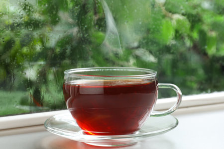 Glass cup of hot tea on windowsill. rainy weatherの写真素材