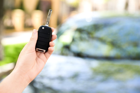 Woman holding key near new car outdoors, closeup. Space for textの写真素材
