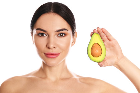 Young woman with silky skin after face mask holding avocado on white backgroundの写真素材