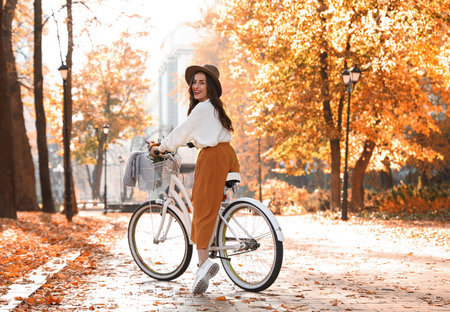 Beautiful happy woman riding bicycle in autumn parkの写真素材
