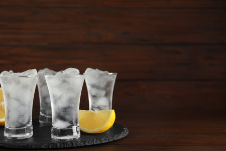 Shot glasses with vodka, ice and lemon on table against wooden background. Space for textの写真素材