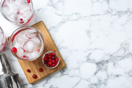 Flat lay composition of cocktail with vodka, ice and cranberry on white marble table. Space for textの写真素材