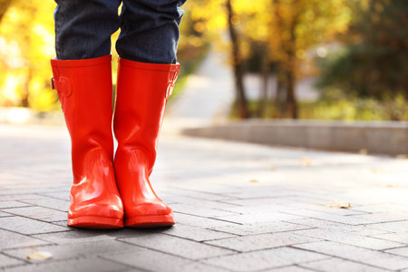 Woman wearing red rubber boots on paved street in park, closeup. autumn walkの写真素材