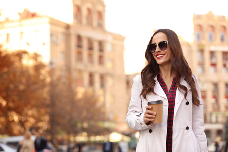 Beautiful woman with cup of coffee on city street. autumn walkの写真素材