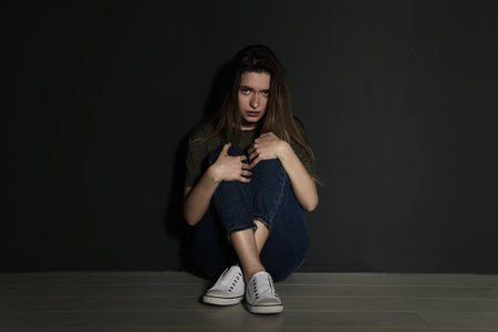 Upset young woman sitting on floor near gray wallの写真素材