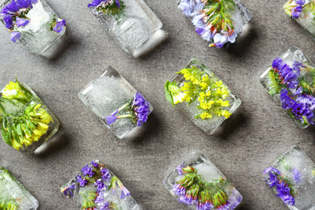 Ice cubes with flowers on gray stone background, flat layの写真素材