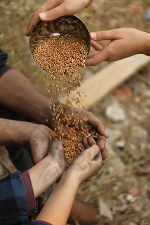 Woman giving poor homeless people bowl of wheat outdoors, closeupの写真素材