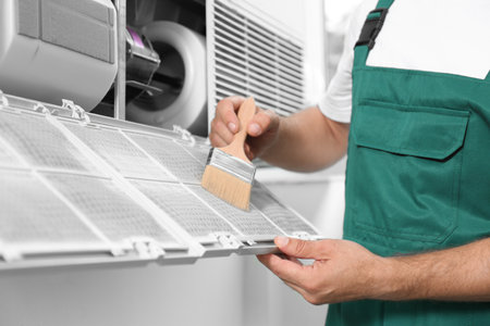 Professional male technician cleaning air conditioner indoors, closeup. Repair and maintenanceの写真素材