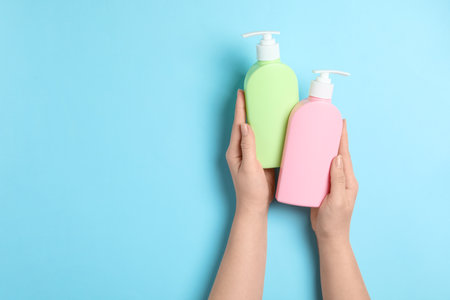 Woman holding blank bottles of cosmetic products on blue background, top view. space for designの写真素材