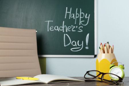 Eyeglasses and stationery on gray table near chalkboard with inscription HAPPY TEACHER'S DAY in classroomの写真素材