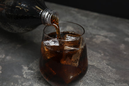 Pouring refreshing soda drink into glass on gray table