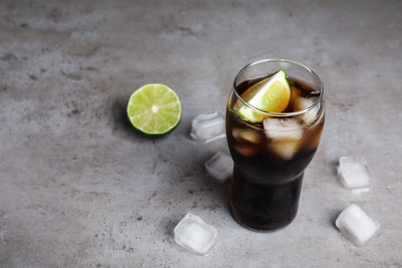Refreshing soda drink, ice cubes and lime on gray table, space for text