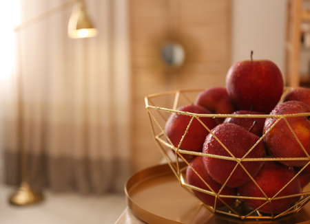Fresh ripe red apples with water drops in decorative basket on table indoors, space for textの写真素材