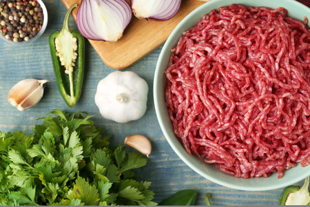 Flat lay composition with bowl of raw minced meat on blue wooden table