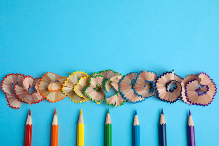 Color pencils and shavings on blue background, flat lay. Space for text