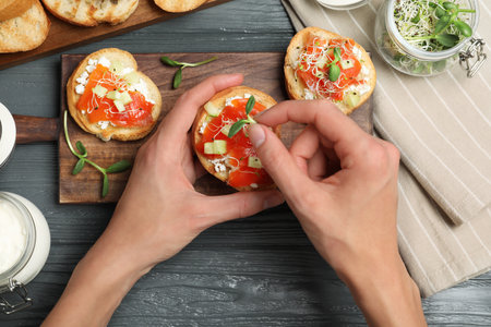 Woman preparing bruschetta with salmon at dark gray wooden table, top viewの写真素材