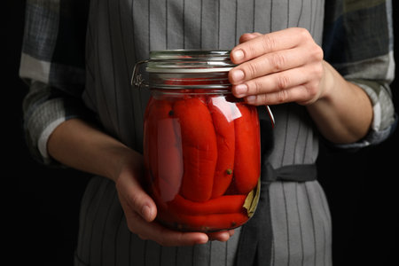 Woman holding jar with pickled peppers against dark background, closeupの写真素材