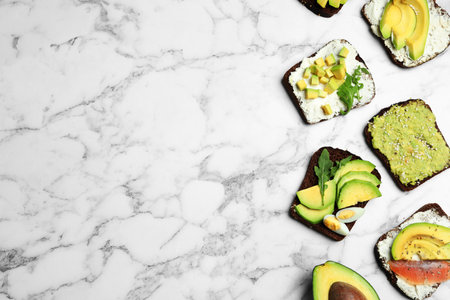 Delicious avocado sandwiches on white marble table, flat lay. Space for text