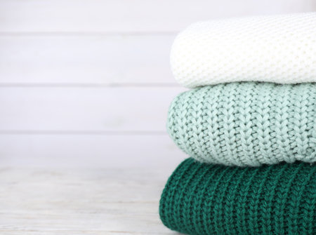Stack of soft knitted sweaters on white wooden table. Space for textの写真素材
