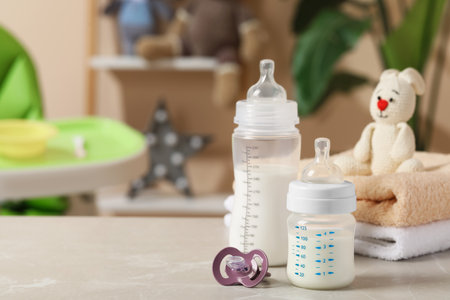 Feeding bottles with baby formula, pacifier and towels on light gray table indoors. Space for text