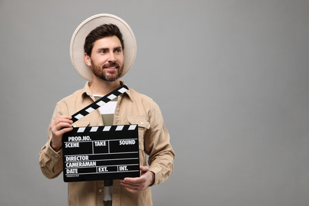 Smiling actor holding clapperboard on gray background, space for textの写真素材
